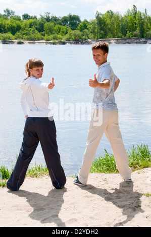 Woman and personal trainer are doing exercises near river Stock Photo