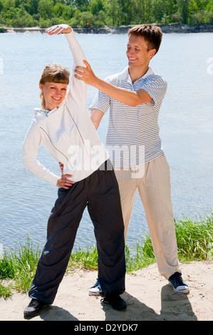 Woman and personal trainer are doing exercises near river Stock Photo