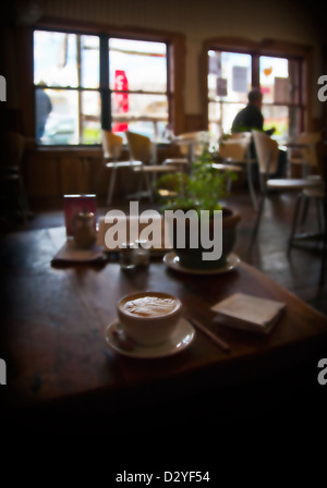 A cup of latte coffee with traditional fern pattern in the foam, on a rustic wooden table. Cafe in North Island, New Zealand Stock Photo