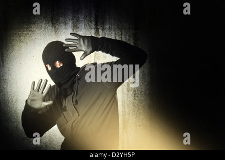 Catch the burglar concept, thief with balaclava caught in front of the grunge concrete wall. Stock Photo