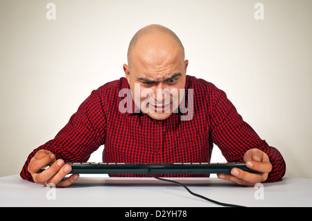 Worried young adult bald man sitting at the office table in front of the computer keyboard Stock Photo