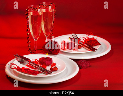Photo of festive table setting, luxury white dishware on red tablecloth, hearts decorations, beautiful rose flower, two glasses Stock Photo
