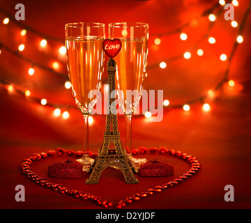 Picture of two glass with champagne decorated with little Eiffel tower and heart-shaped candles and beads on red background Stock Photo