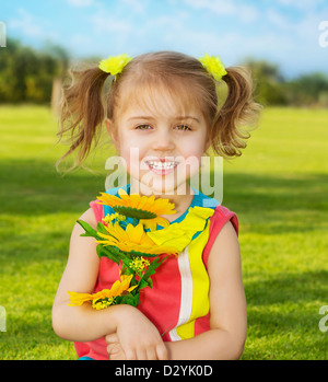 Picture of cute happy little girl wearing colorful dress and holding in hands beautiful sunflower bouquet, adorable small female Stock Photo