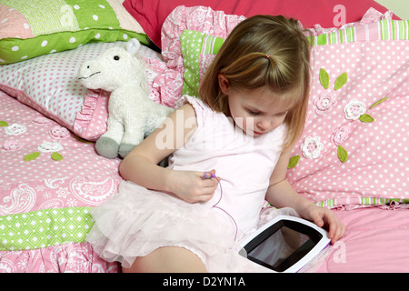 4 year old using an i pad touch screen device in her bedroom Stock Photo