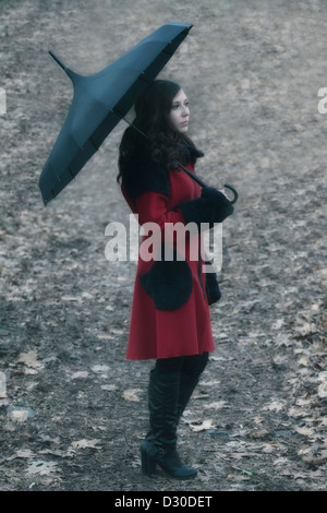 a woman with a red coat and an umbrella is walking on a forest track Stock Photo