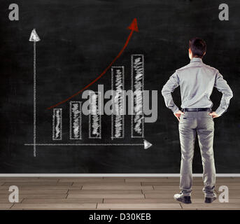 young business man in front of a blackboard presenting a trend business chart Stock Photo