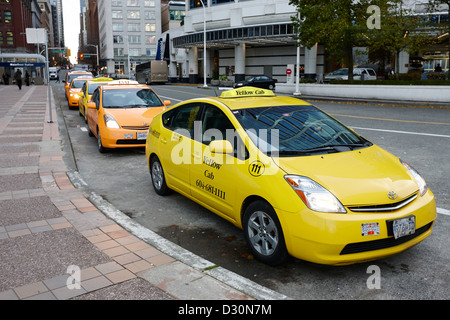 row of yellow cabs outside canada place including prius hybrid vehicles Vancouver BC Canada Stock Photo