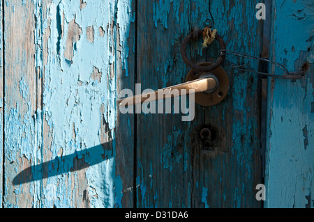 An old wooden painted door with a metal handle and tie ring with a loop of wire attached to hook to keep it shut. Stock Photo
