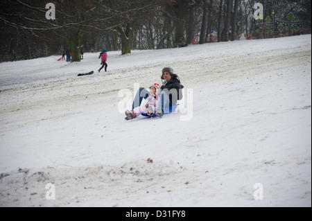 An Adult and small child on a sledge or toboggan going downhill in a snow covered landscape. Stock Photo