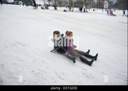 Two young teenage girls on a sledge or toboggan going down hill at speed in the snow. Stock Photo