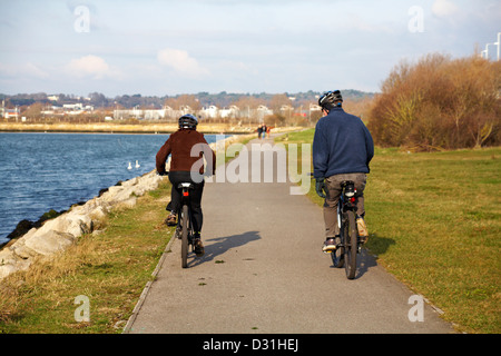 Couple riding their bikes along path around Holes Bay, Poole Harbour in January Stock Photo