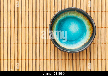 small empty ceramic bowl (sauce dish) with blue enamel on bamboo place mat Stock Photo