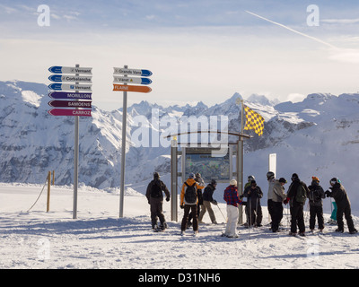 Skiers by piste map, direction signs and avalanche warning flag showing level 3 risk in Le Grand Massif ski area in French Alps Stock Photo