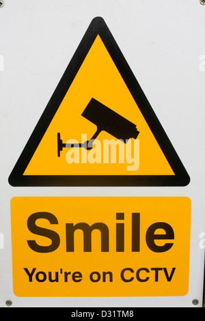 'Smile You're on CCTV' sign with surveillance camera on yellow background in black triangle Denbigh Wales UK Stock Photo
