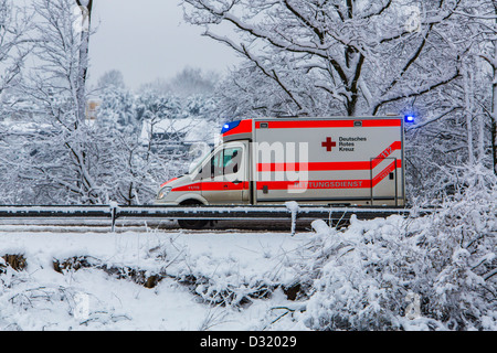 Ambulance of the German Red Cross. At a emergency operation, with lights flashing, on a snowy street in winter Stock Photo