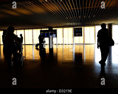 Passengers in an airport on their way to catch flights with screens showing departure information Stock Photo