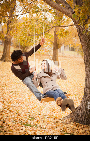 Couple playing on swing in autumn leaves Stock Photo