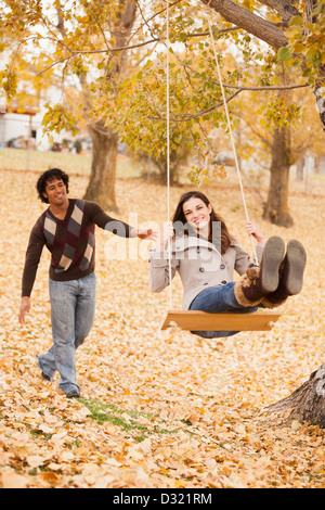 Couple playing on swing in autumn leaves Stock Photo