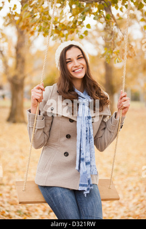 Caucasian woman sitting on swing in autumn leaves Stock Photo