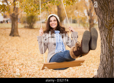 Caucasian woman sitting on swing in autumn leaves