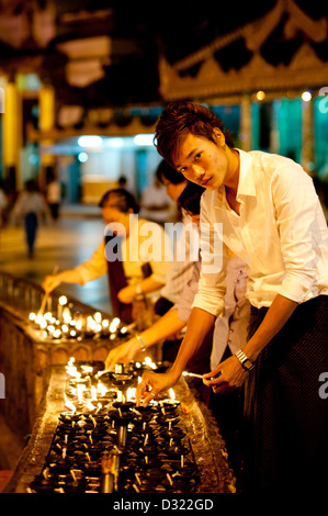 A young man lights oil lamps in prayer at Shwedagon Pagoda, Yangon, Burma (Myanmar) Stock Photo