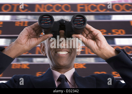 Smiling mixed race businessman using binoculars Stock Photo