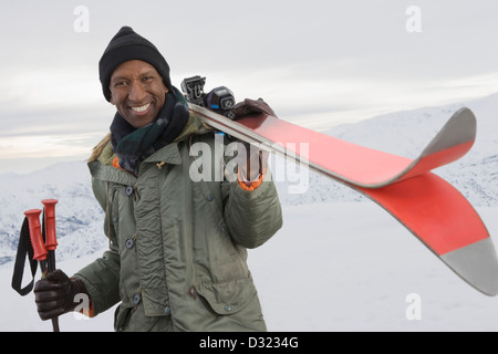 Mixed race man carrying skis on snowy slope Stock Photo