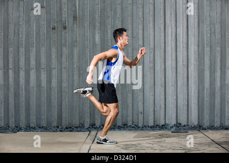 Athlete Chinese man running in urban city. Asian Runner jogging outdoors with a wall in background. Male fitness concept. Stock Photo