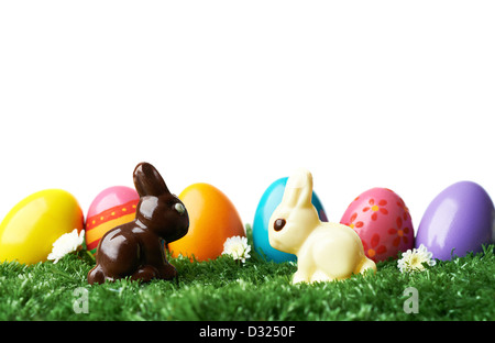 Row of colored and decorated Easter eggs in grass with two chocolate rabbits in front Stock Photo