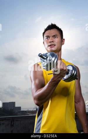 Athletic Young Chinese man exercising with dumbbells. Muscular Asian man exercising with weight training equipment. Stock Photo