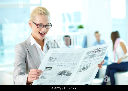 Portrait of amazed female looking surprisingly at newspaper in working environment Stock Photo