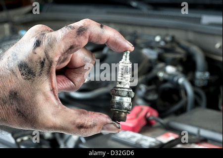 An auto mechanic holds an old, dirty spark plug over a car engine he is tuning up. Stock Photo