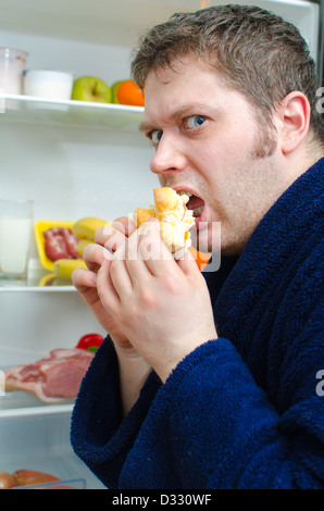 Handsome man eating piece of cake near open fridge Stock Photo