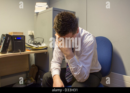 Man hangs head in hands with stress at work, surrounded by clutter. Stock Photo