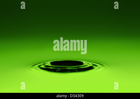 A close-up view of a water surface with a central ripple pattern, created by a drop impact. The surface is illuminated with a smooth green gradient, transitioning from dark green at the top to bright Stock Photo