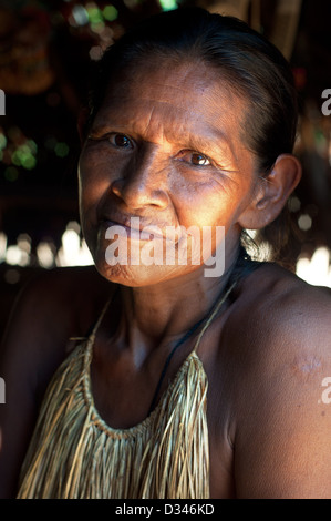 A Yagua elder woman with traditional thatch vest inside a maloca, surroundings of Iquitos, Amazonian Peru Stock Photo