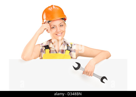 A smiling female worker holding a wrench and standing behind blank panel isolated on white Stock Photo