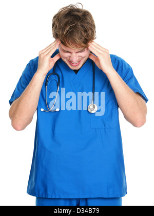 Stressed young male medical professional in blue scrubs touching head in pain isolated on white background Stock Photo