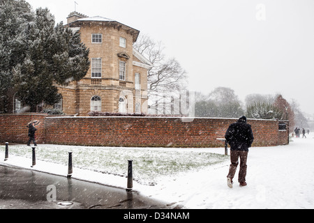 Man walking through falling snow near Asgill House on the Banks of the River Thames, Richmond upon Thames, Surrey Stock Photo