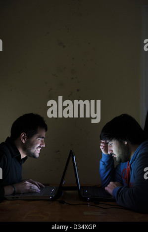 Two young men using laptop computers face to face Stock Photo