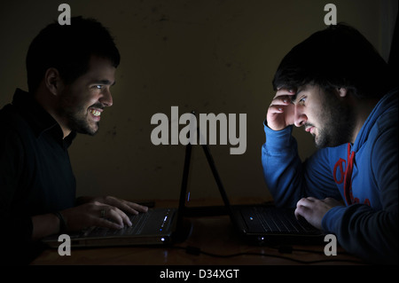 Two young men using laptop computers face to face Stock Photo