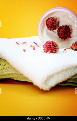 Spa essentials (cream, white towel and flowers) isolated on yellow Stock Photo