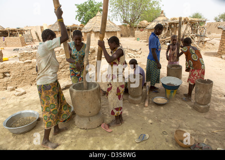 Barsalogho, Burkina Faso, May 2012: Village women and girl pounding grain to prepare family meals. Stock Photo