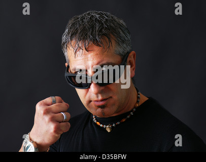 Angry tough guy or criminal with dark biker sun glasses staring at viewer and threatening him with his closed fist. Stock Photo