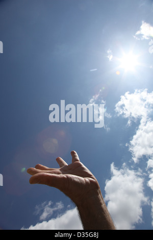 A male hand reaches up to the sun burning bright in the sky, palm facing upwards. Stock Photo