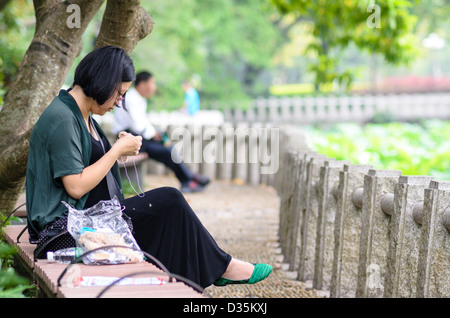Chinese woman carrying out her hobby - sewing - in a public park Stock Photo