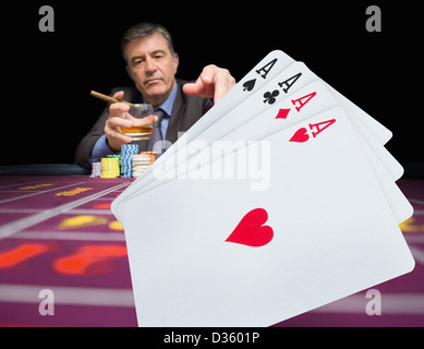 Gambler holding whiskey at poker table with digital hand of cards in foreground Stock Photo