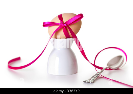 Easter egg with pink ribbon on white background. Composition with silver teaspoon and egg hand painted a beige paint Stock Photo
