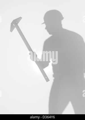 one man construction worker with hardhat and a t square ruler in his hand, standing, silhouette, behind a diffuse surface Stock Photo